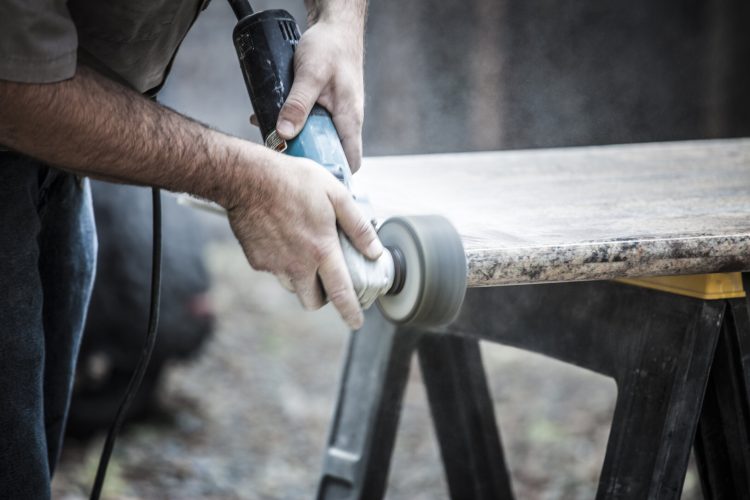 Remodeling home with granite counter tops. Man polishing granite counter tops outdoors.